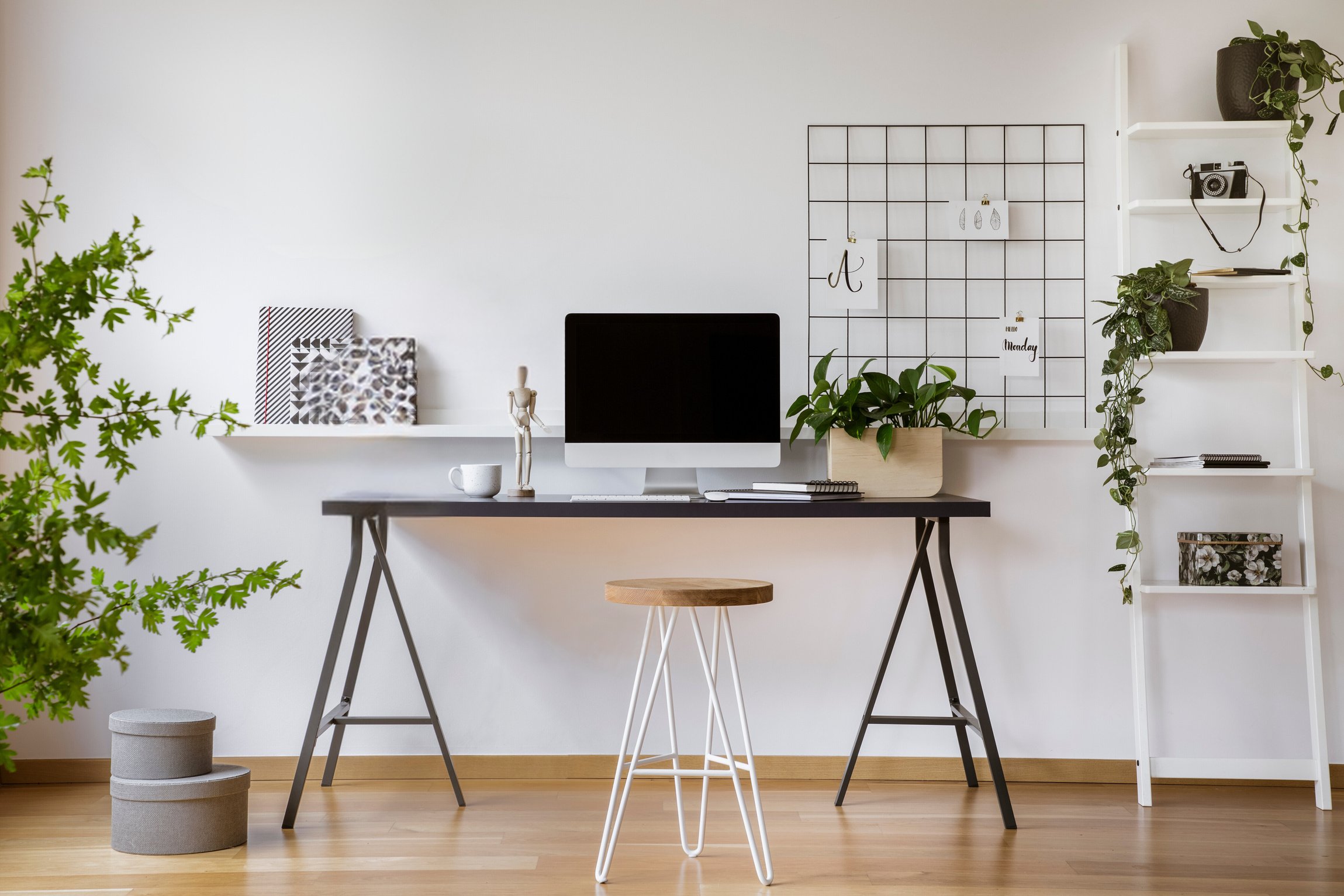 Hairpin stool standing by the wooden desk with mockup computer screen, metal lamp and coffee cup in real photo of white home office interior